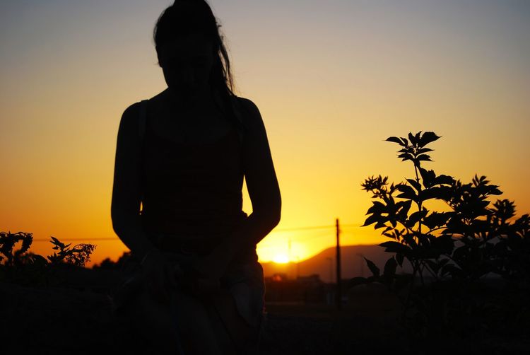 Silhouette woman standing by tree against sky during sunset