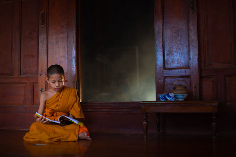 Full length of boy wearing traditional clothing reading book while sitting on floor