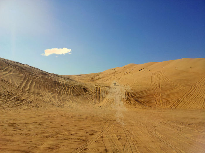 A 4wd driving through dusty oman desert rub al khali sand dunes with blue sky
