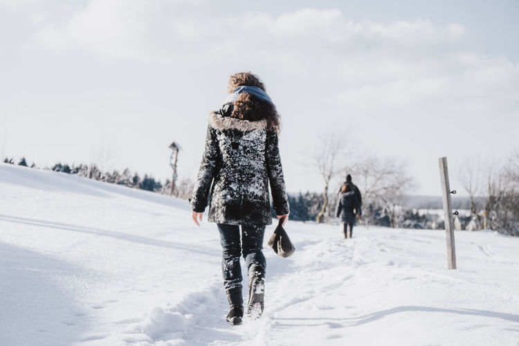 Rear view of woman walking on snow covered field