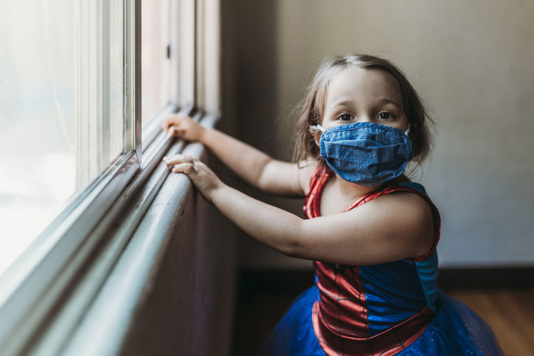 Preschool age girl by window in halloween costume and face mask