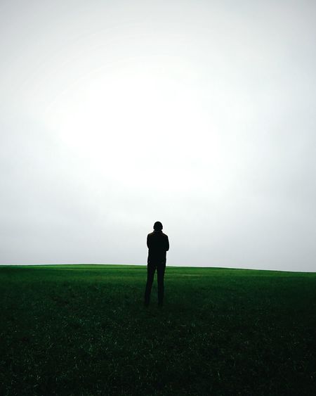 Rear view of silhouette man standing on field against clear sky