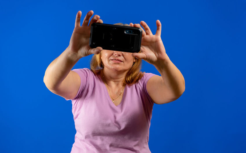 Woman holding camera while standing against blue sky
