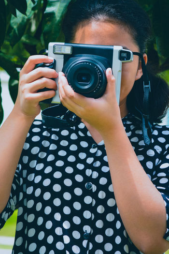 A girl wearing a polkadot dress holding an slr camera obscuring her face 