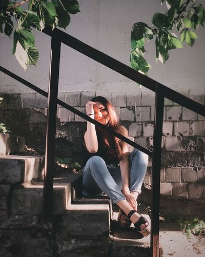 Woman looking away while sitting on steps by wall