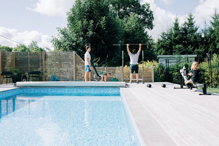 Two men and their children working out at the home gym by the pool