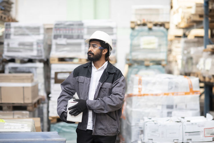 Young man wearing hard hat working in a warehouse carrying a box