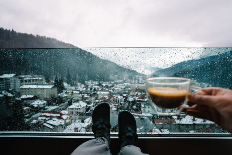 Low section of woman with drink in balcony at mountains against sky