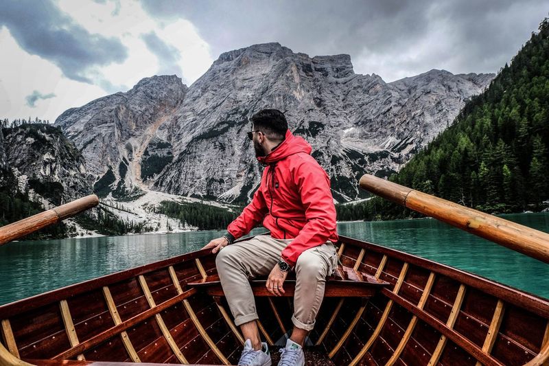 Man sitting on boat in lake against mountains and sky