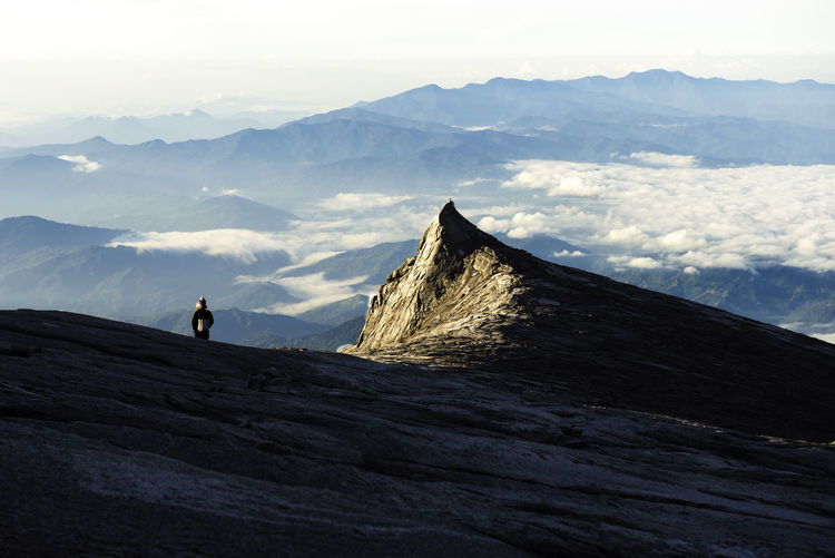 Distant view of man standing on mountain against sky