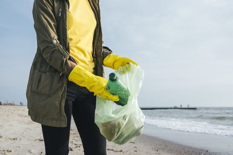 Woman wearing gloves collecting waste plastic bottles in garbage bag