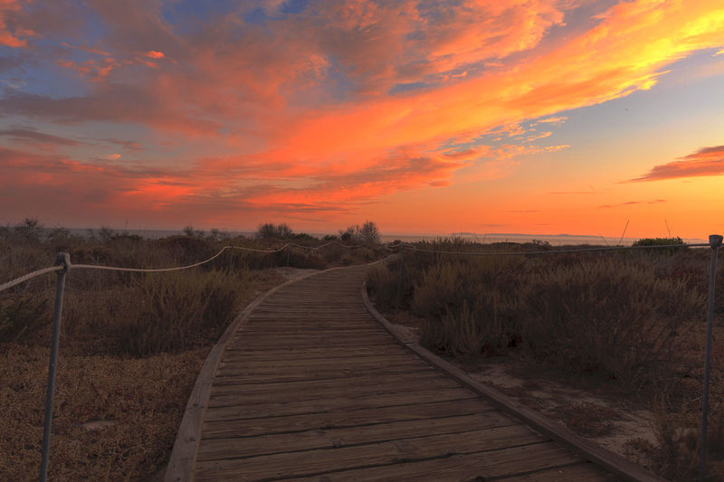 Boardwalk against cloudy sky during sunset