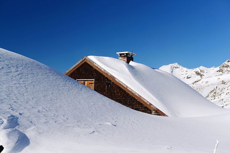 Snow covered house at mountain against clear blue sky