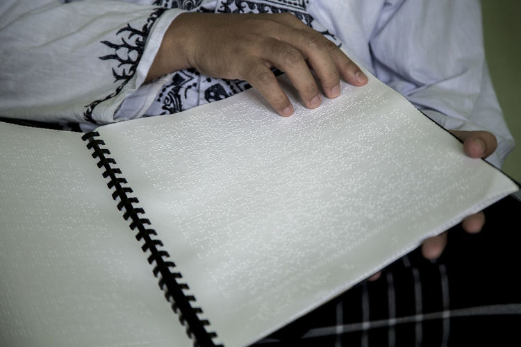 Midsection of blind person reading bible in braille