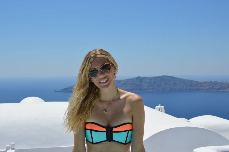Young woman wearing sunglasses standing at beach against clear blue sky