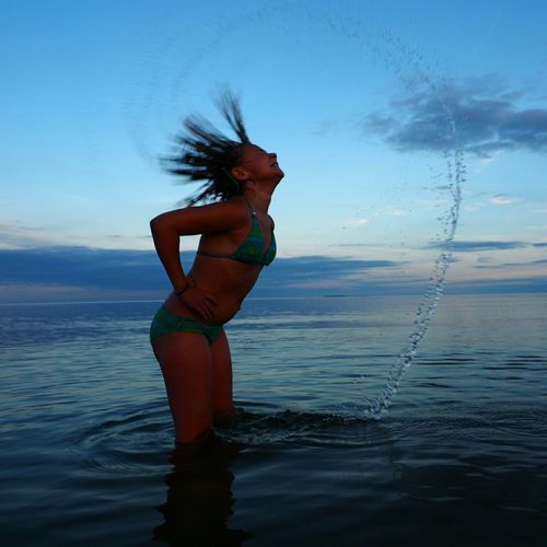 Woman in bikini with tousled hair at baltic sea against sky at dusk