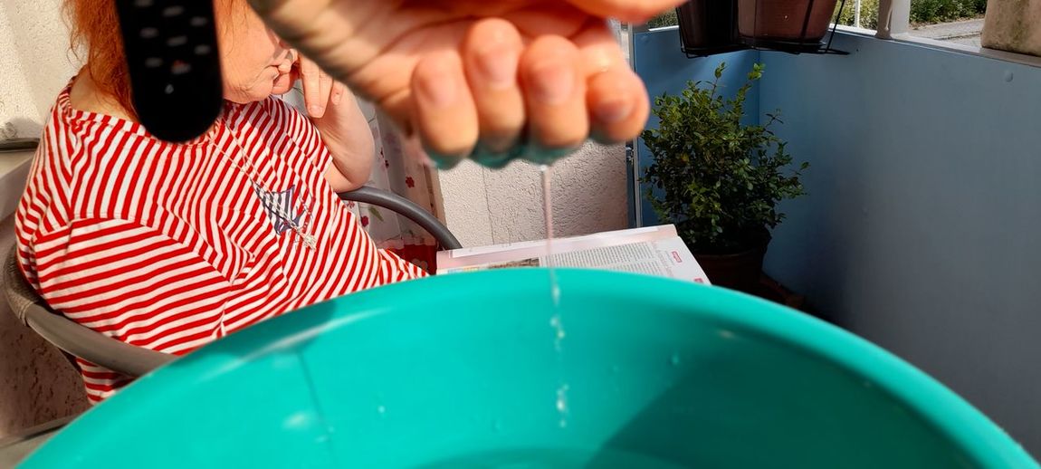 Close-up of water falling from hand in bucket with girl studying at background