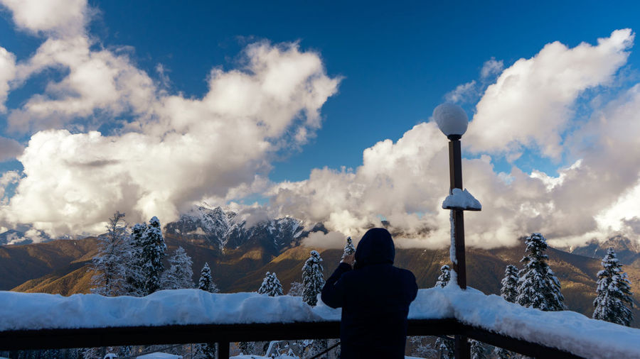Rear view of person standing on snow covered mountain against sky