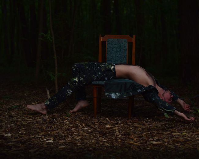 Side view of young man lying on chair in forest