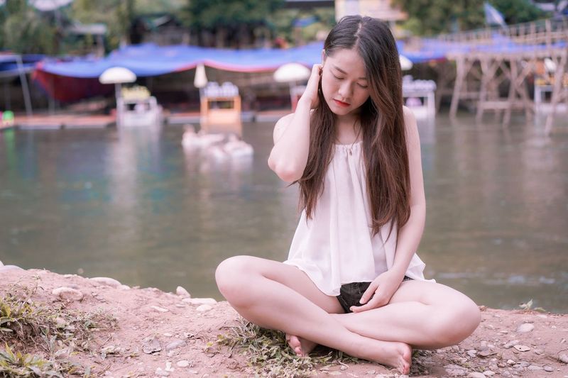 Beautiful young woman sitting against lake