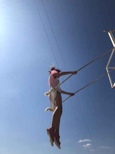 Low angle view of girl sitting on swing against blue sky