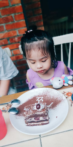 Cute girl sitting by cake at home