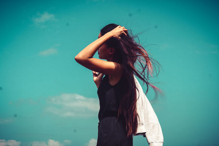 Young woman standing against blue sky