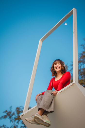 Portrait of smiling young woman sitting against blue sky