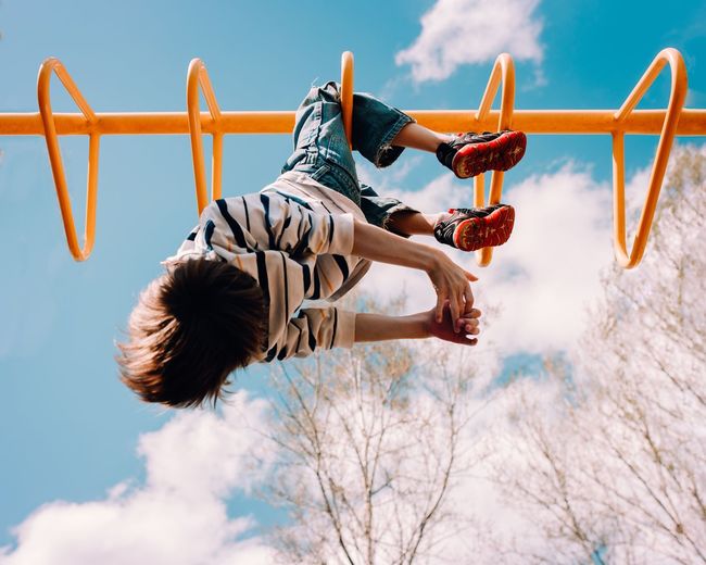 Low angle view of boy playing on monkey bars against sky