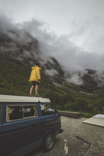 Rear view of man standing by mountain on vehicle during foggy weather