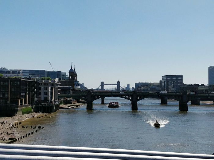 Bridge over river by buildings against clear sky