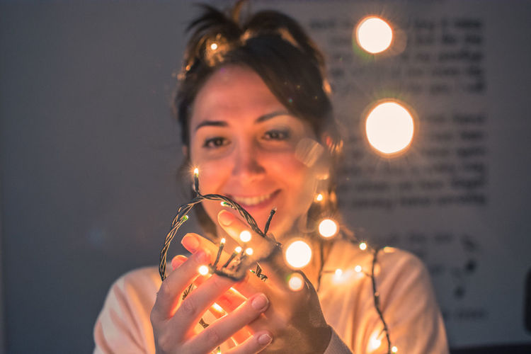 Smiling woman holding illuminated lights in darkroom