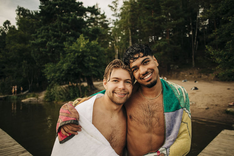 Portrait of young man with arm around male friend wearing towel during vacation