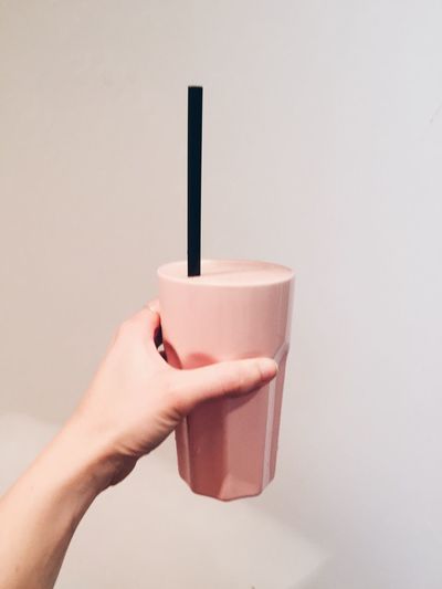 Cropped hand holding glass of smoothie against white background