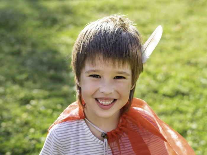 Smiling boy playing american indian. kid with white bird feather and red cloak. costume role play. 