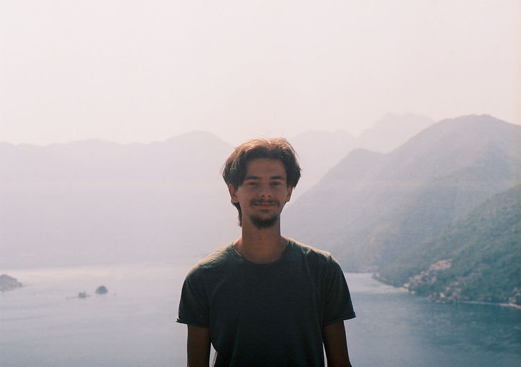 Portrait of young man standing on mountain against sky