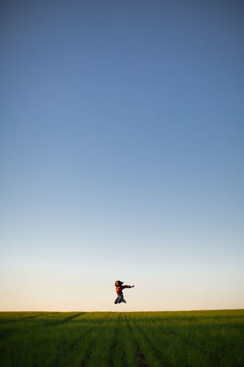 Girl jumping on farm against clear blue sky