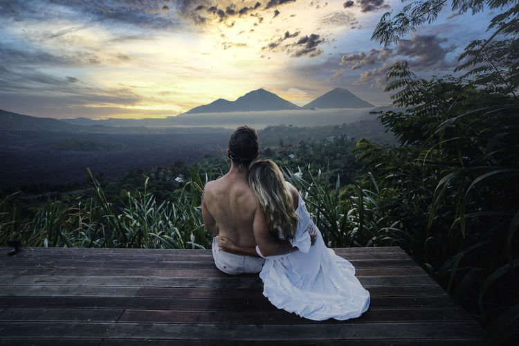 Rear view of couple sitting on mountain against sky