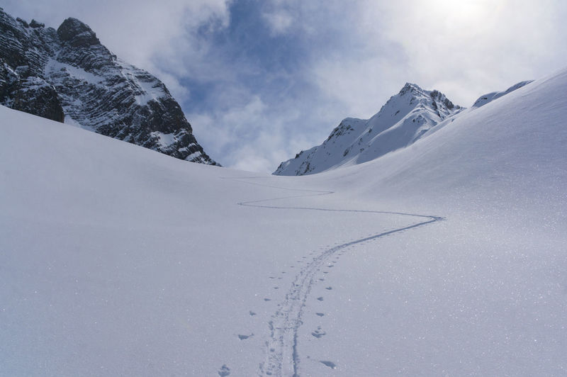 Ski track on snowcapped mountain against sky