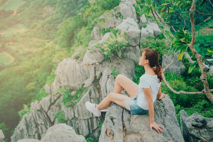 Young woman sitting on rock against trees