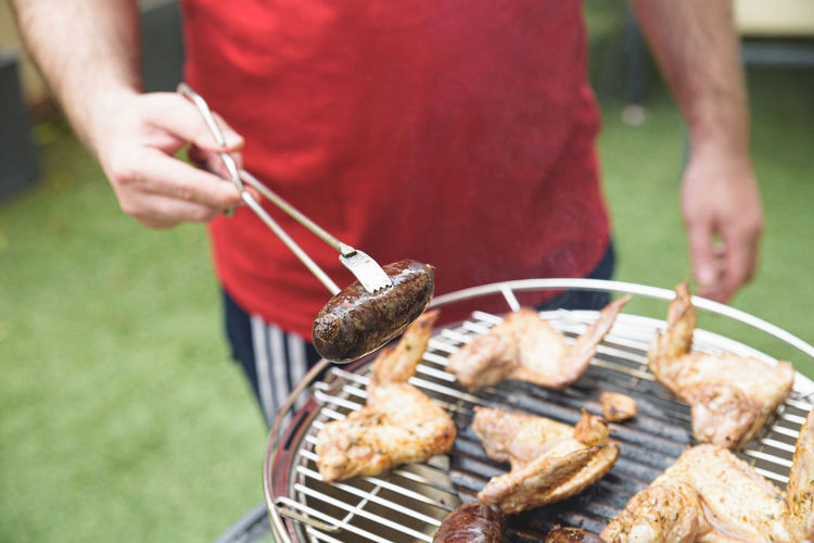 Midsection of man preparing meat on barbecue grill