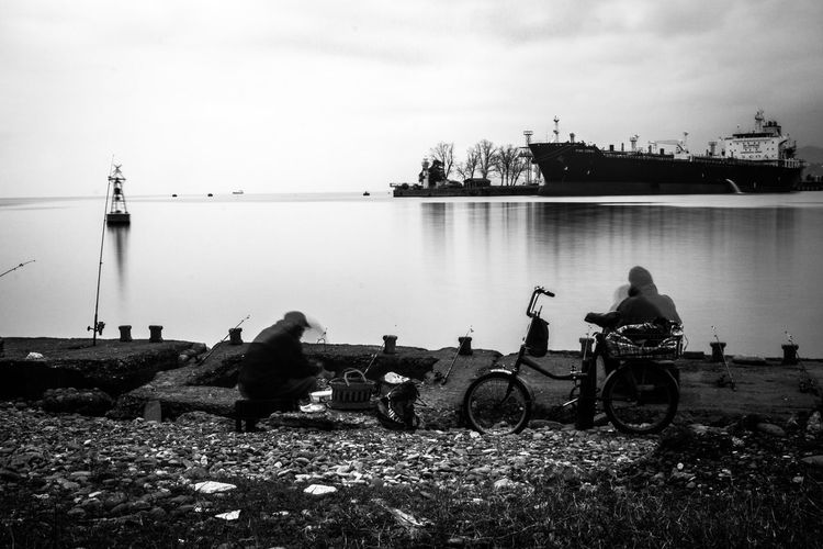 Men sitting on shore against sky