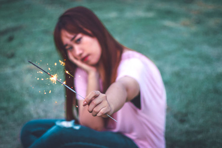 Portrait of woman holding sparkler while sitting on grass