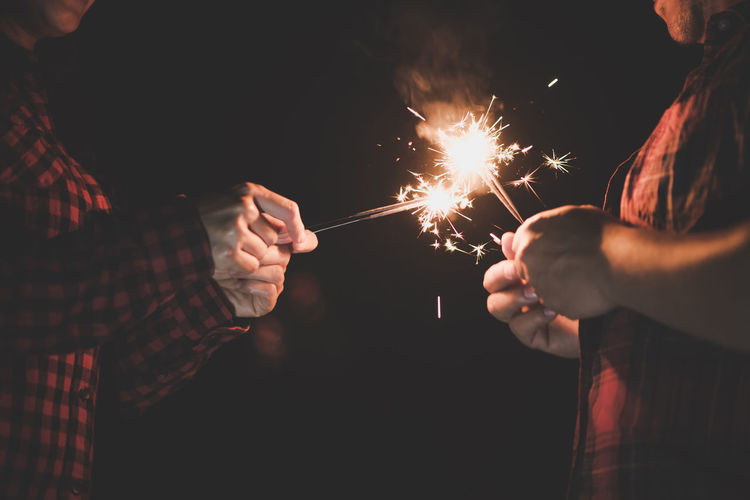 Midsection of people holding sparklers at night