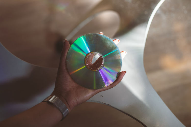 Cropped hand of woman holding compact disc at glass table