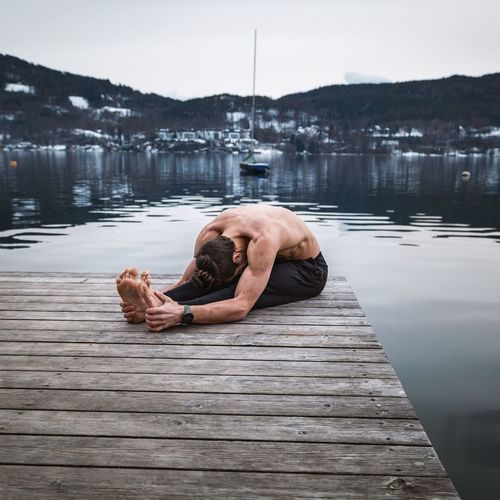 Man lying on pier over lake against sky