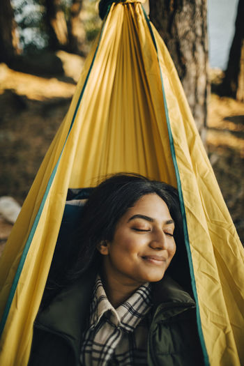 Smiling woman with closed eyes on hammock in forest during vacation