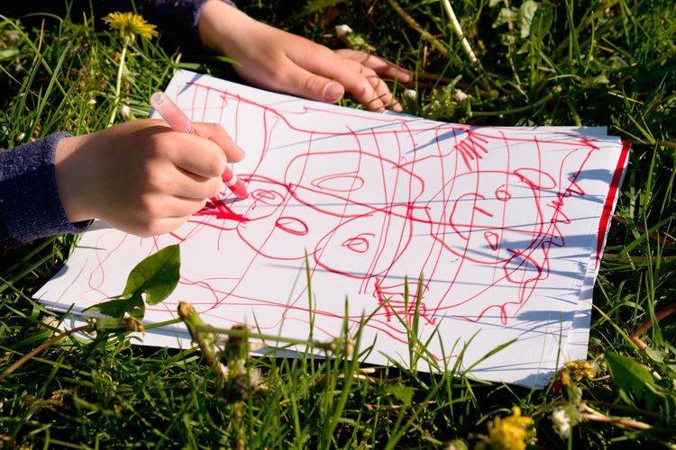 Close up view of child's hand drawing colorful ornaments on paper. notebook in  grass of meadow.