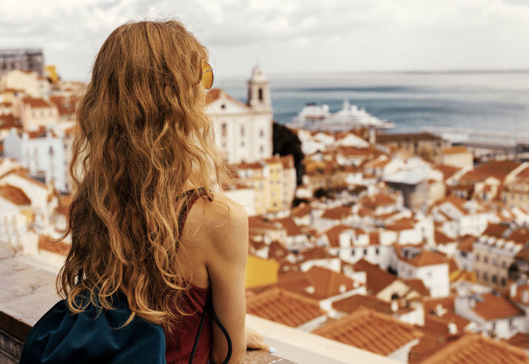 Rear view of woman standing over buildings against sea and sky