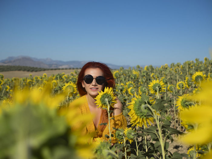 Portrait of young woman standing amidst yellow flowering plants against sky